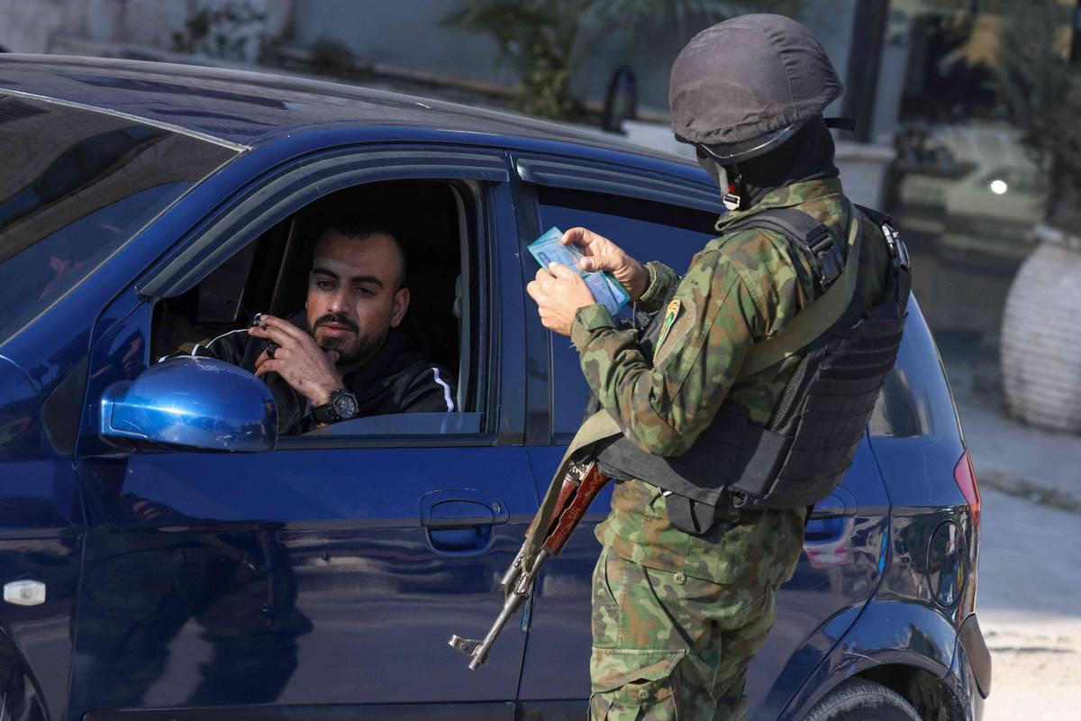 شرطي فلسطيني يدقق هوية شخص عند مدخل مخيم جنين