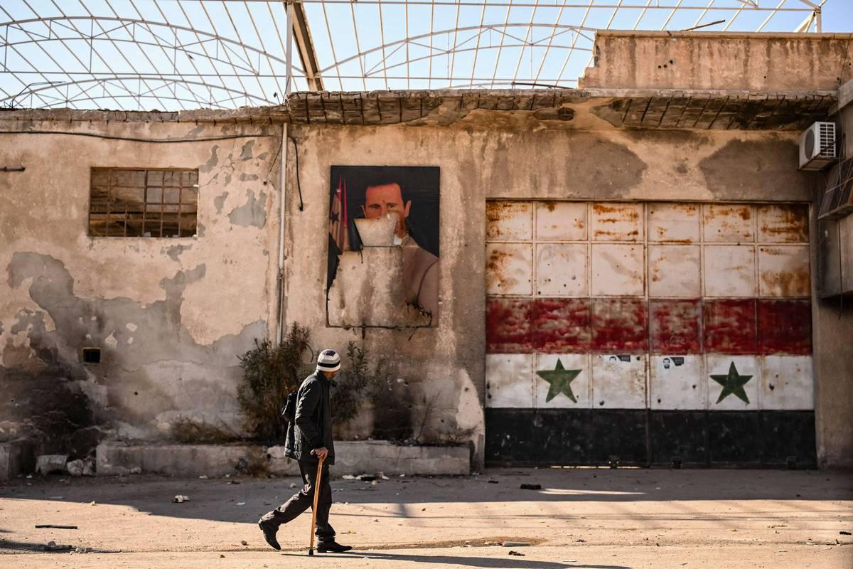 سوري أمام صورة مشوهة للرئيس السابق بشار الأسد جنوب دمشق