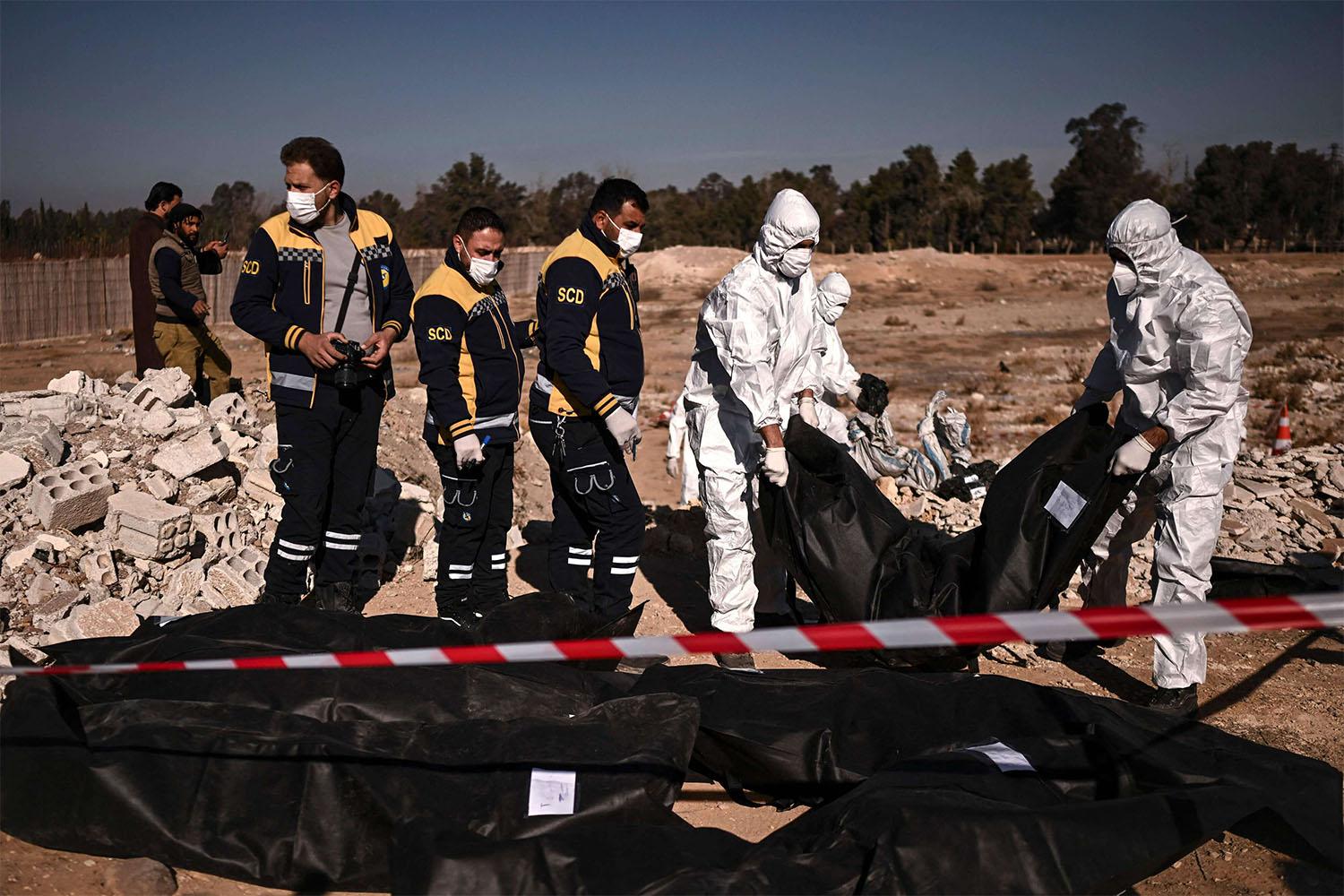 Members of Syria's White Helmets civil defence transport body-bags containing human remains that were recovered from a mass grave in Damascus
