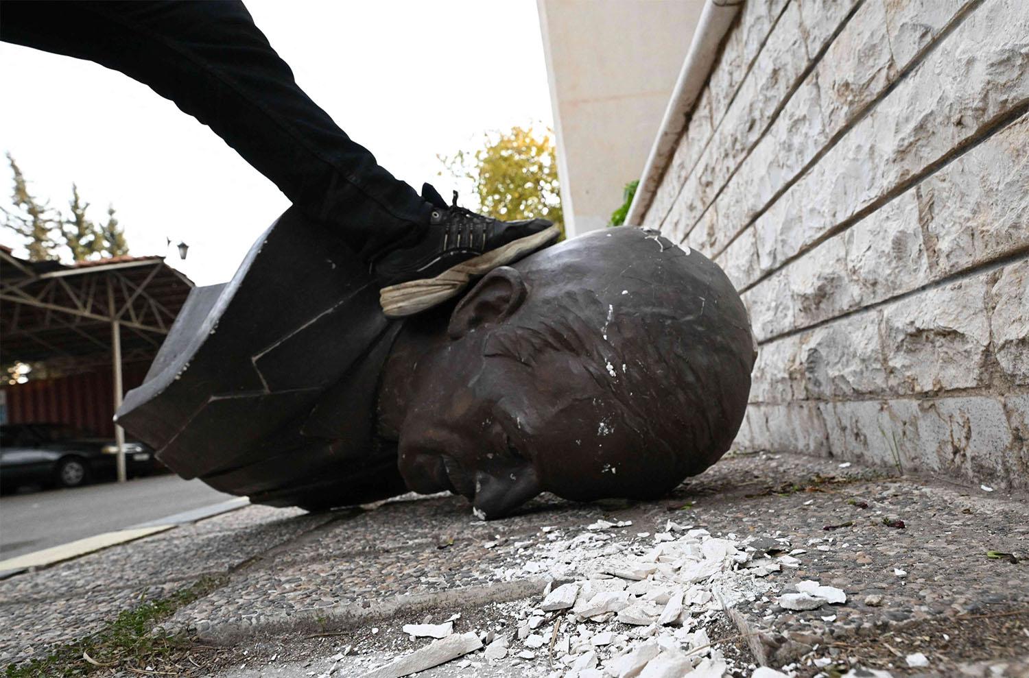 An anti-government fighter steps on the head of a broken statue of late Syrian president Hafez al-Assad