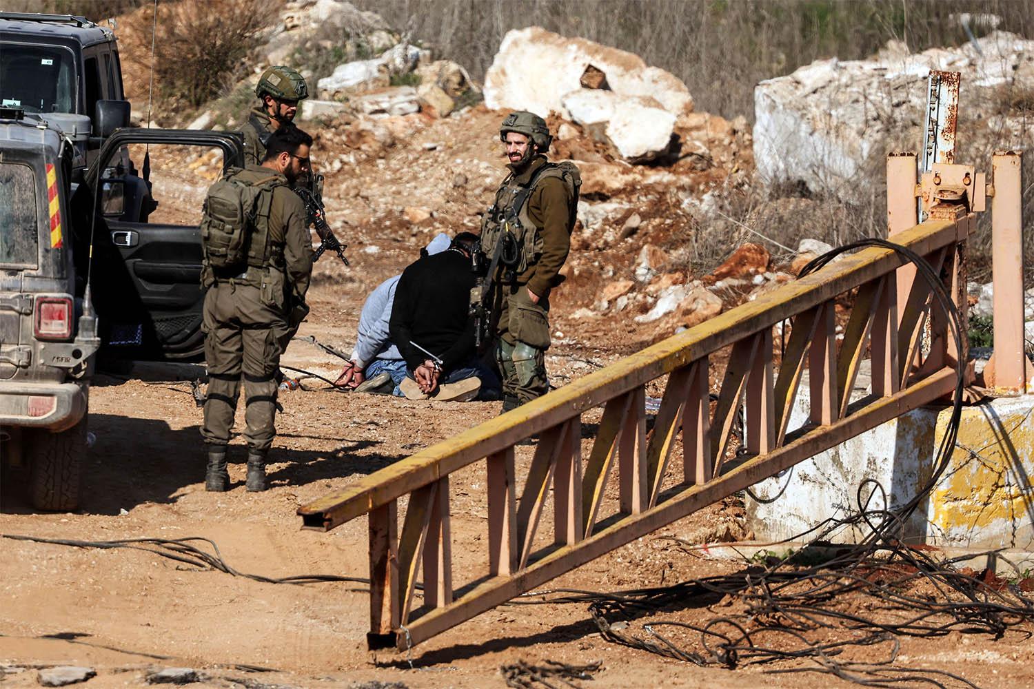 Israeli soldiers stand near Lebanese detainees at the Israeli-Lebanese border