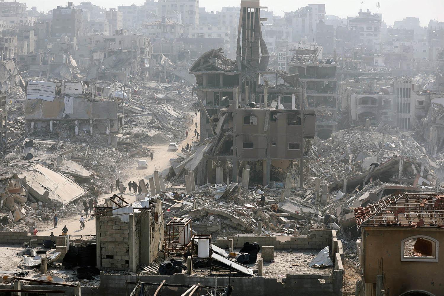 People walk past the rubble of destroyed buildings in Jabalia