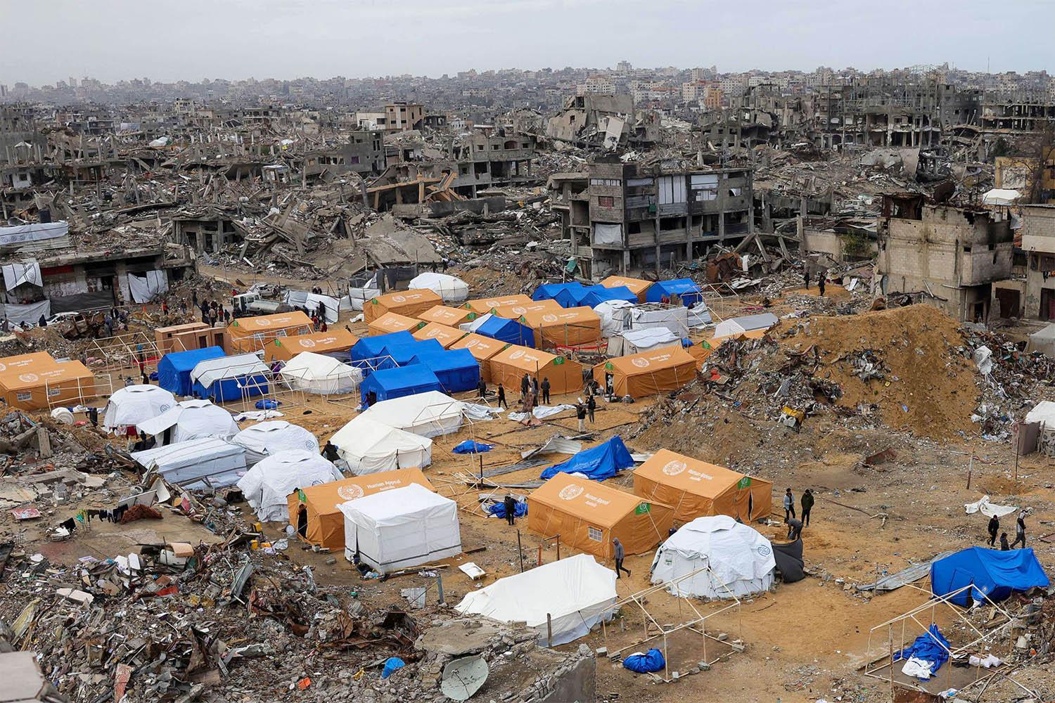 Palestinians walk around their tents, set up amid heavily damaged buildings in Jabalia