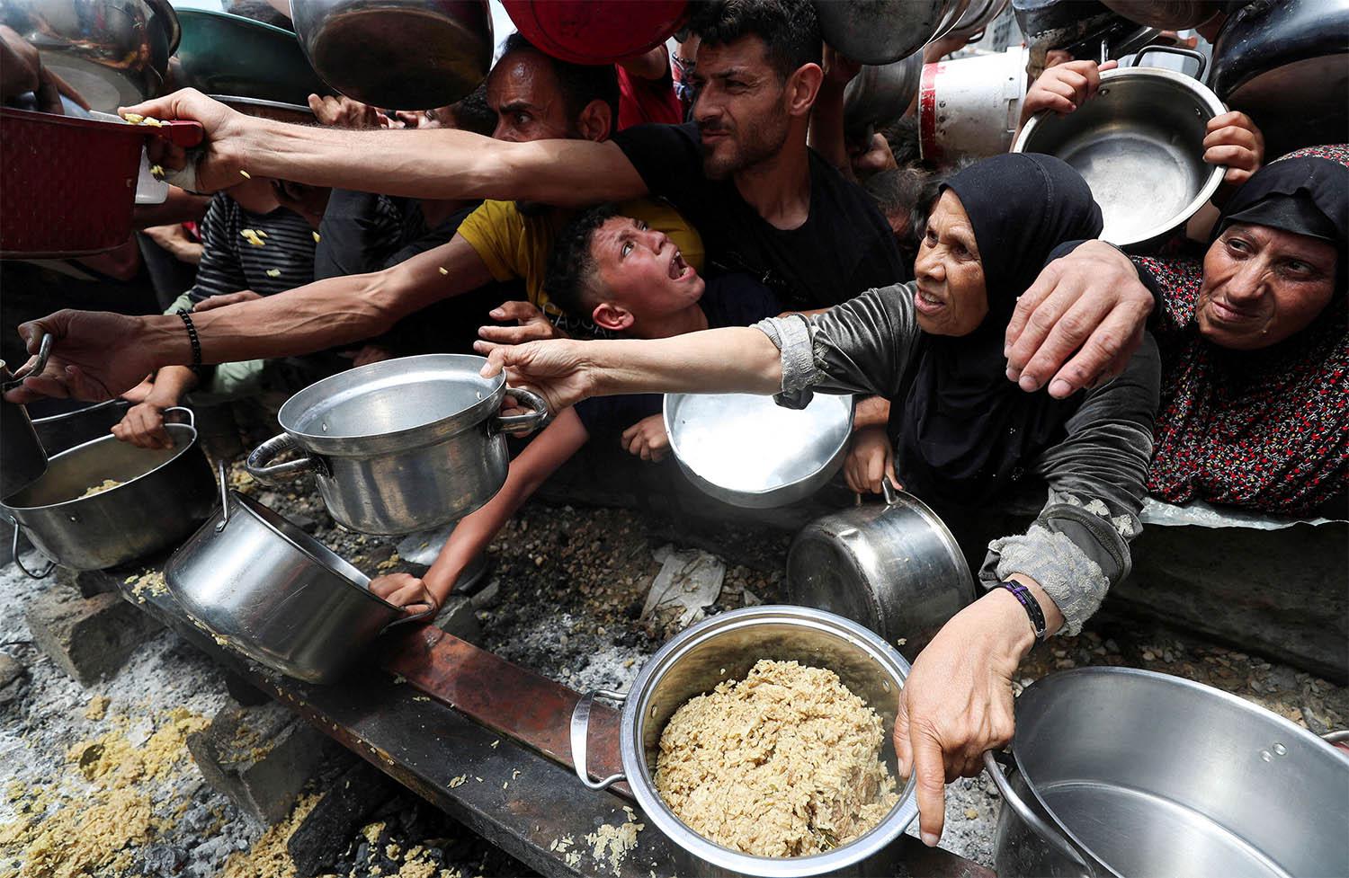 Palestinians wait to receive food cooked by a charity kitchen in Jabalia
