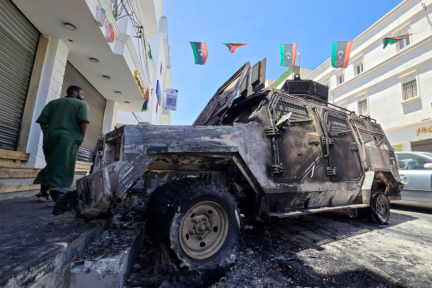 A man walks past a car that was destroyed during overnight clashes in the southern district of Abu Salim in Tripoli