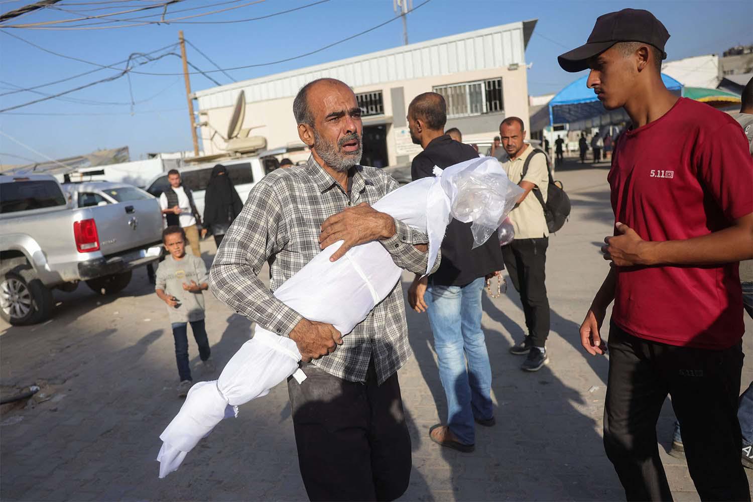 A Palestinian man carries the draped body of a child killed in Israeli strikes the previous day on the central Gaza Strip, outside the Shuhada al-Aqsa hospital