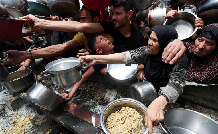 Palestinians wait to receive food cooked by a charity kitchen in Jabalia