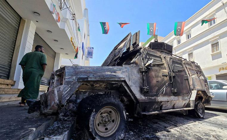A man walks past a car that was destroyed during overnight clashes in the southern district of Abu Salim in Tripoli